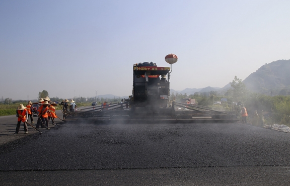 2019年8月，宜春經(jīng)開區(qū)S311路面攤鋪現(xiàn)場(chǎng)，工友們輔助路面兩側(cè)的分料、補(bǔ)窩等作業(yè)